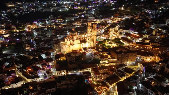Aerial orbit hyperlapse revealing Taxco, Mexico, at night with its lights and the Parish Church of Santa Prisca and San Sebastian, a tourist attraction with colonial architecture
