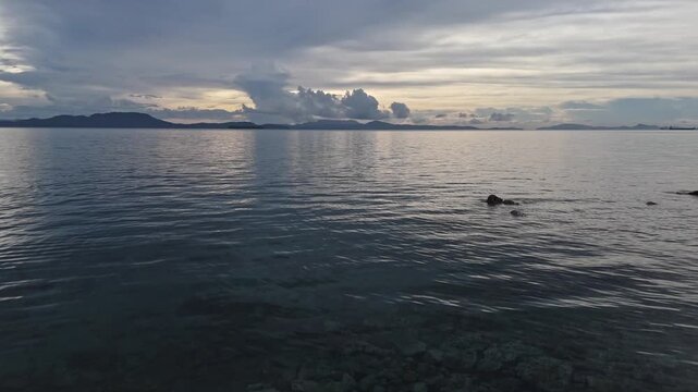 Wide seascape from Punta Bilar Surigao City Philippines showing a tranquil sea at dusk with silhouetted island mountains in the distance under a dramatic cloudy sky with warm light on the horizon.