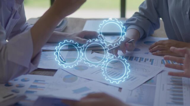 Business people discussing financial charts with digital gears overlay, representing teamwork, data analysis, workflow automation and business process planning.