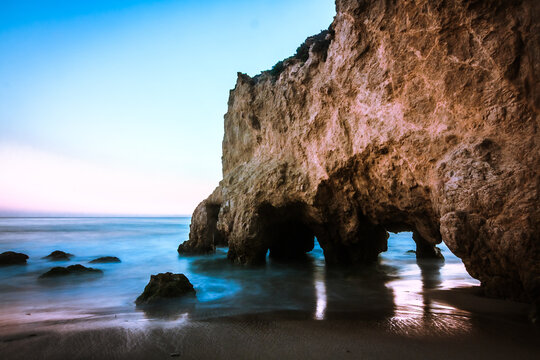 View of a sea cave and rock formations at the shoreline with gentle waves and soft light in Malibu, California, United States.