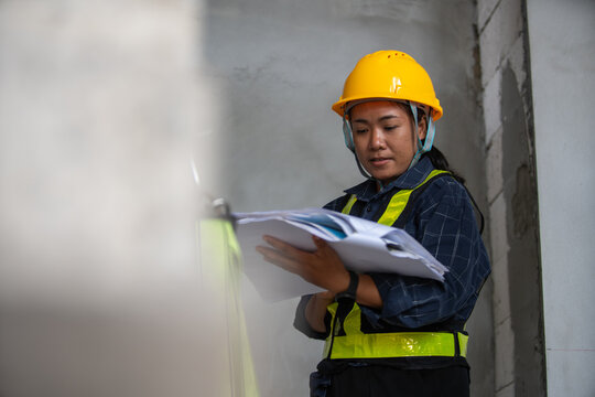Female construction worker reviewing project plans on job site with safety gear and attention to detail