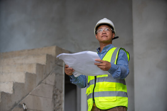 Confident construction engineer reviewing plans on a job site with safety gear and high visibility vest