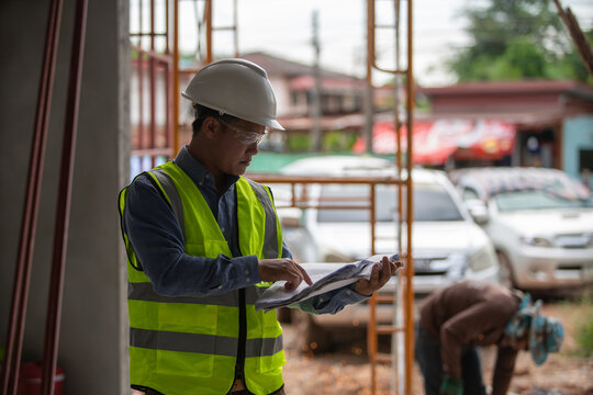 Construction worker wearing safety equipment examining blueprints at a job site with scaffolding visible in the background