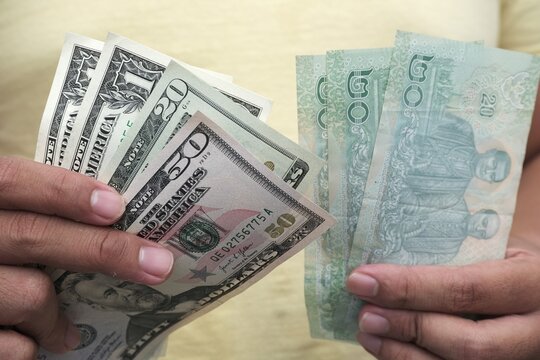 Close-up of hands holding Thai baht and US dollar banknotes, showing currency exchange, travel finance, and money comparison.