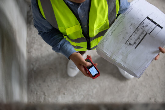 Construction worker examining blueprints and utilizing technology for effective project management at a building site