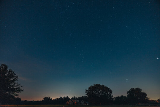 View of a starry night sky over a silhouette of trees and a residential house in the countryside in Tampa, Florida, United States.