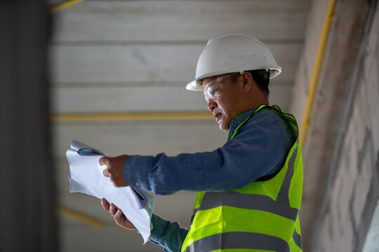 Construction worker reviewing architectural plans at a construction site while wearing protective safety equipment