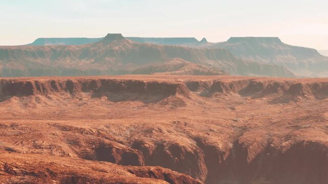 A wide view of a rocky landscape featuring large mesas and deep valleys under warm sunlight. The terrain has various textures and colors, showcasing natural erosion patterns.