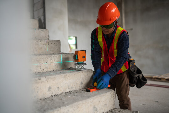 Construction worker using laser level tool on staircase at construction site for accurate measurements