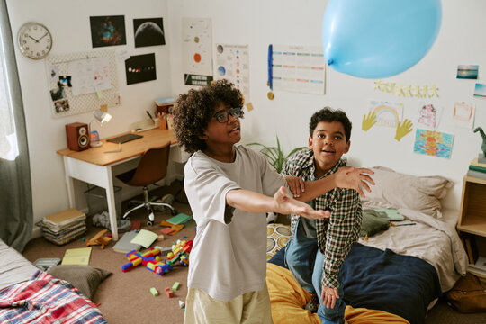 High angle shot of two boys playing with balloon in bedroom, moving actively and bonding through indoor fun. Suitable for family lifestyle, childhood, sibling, home activity campaigns