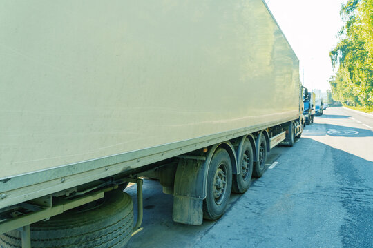 View along the side of a large white articulated trailer parked at the edge of a paved rural road. Visible details include the trailer wheels and mudflaps