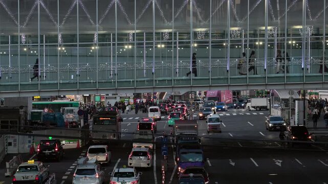 Twilight in Tokyo : Commuters Walk along a Pedestrian Skywalk Spanning a Busy Street in Front of Shibuya Station, Bustling with Neon Lights and Headlights Shining on the City | Shibuya, Tokyo, Japan