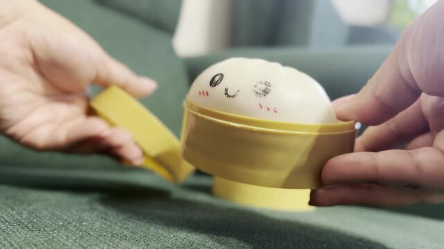 Hands placing an egg in a yellow cup on a sofa