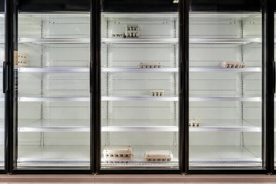 Empty supermarket refrigerator shelves with scattered egg cartons, symbolizing food scarcity, economic crisis, and supply chain issues