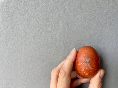Close-up photograph of a fresh brown chicken egg with a feather attached to the shell, held in a hand against a neutral grey background. Natural farm-to-table concept representing fresh produce, 