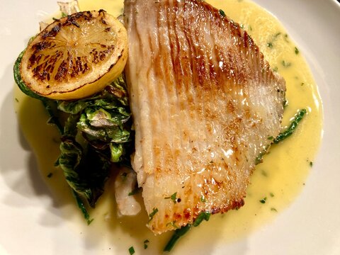 Pan-seared skate wing served with a rich creamy herb sauce, charred lemon, and seasonal green vegetables. Elegant seafood main course beautifully presented on a white plate, ideal for fine dining, res