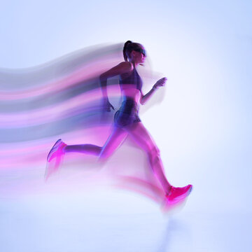 Female runner sprinting with colorful motion blur in modern studio scene. Concept of marathon events, running clubs, wellness programs, health campaigns, wearable technology.