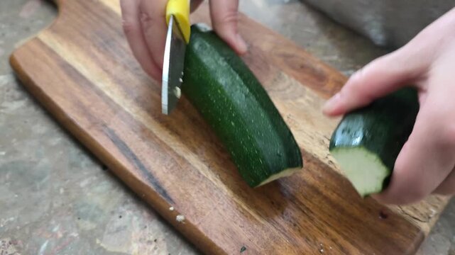 Young green zucchini are cut with a knife on a wooden board on the table