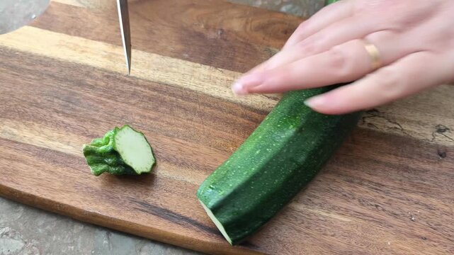 Young green zucchini are cut with a knife on a wooden board on the table