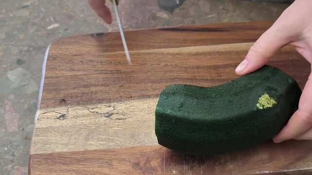 Young green zucchini are cut with a knife on a wooden board on the table