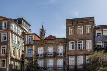 Obraz premium Vista frontal de hermosas fachadas históricas decoradas con azulejos típicos, balcones con flores y ventanas clásicas, con la Torre de los Clérigos asomando al fondo bajo un cielo despejado en Portuga