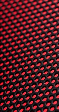 Perforated metal with red holes. Close-up repeating pattern of circular perforations in black metal sheet with vibrant red backlighting glow, slow subtle camera movement across the surface.