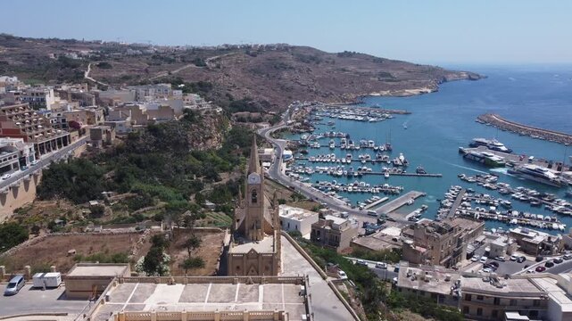 Drone view of Mgarr harbour in Gozo Island, Malta. Church of the Madonna of Lourdes in the foreground . High quality 4k footage