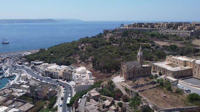 Drone view of Mgarr harbour in Gozo Island, Malta. Church of the Madonna of Lourdes on the right and Fort Chambray on top of the hill. High quality 4k footage