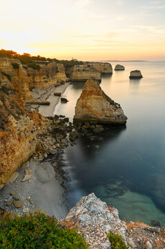 View of the rugged limestone cliffs and sea stacks along the golden coastline at sunset in Algarve, Portugal.