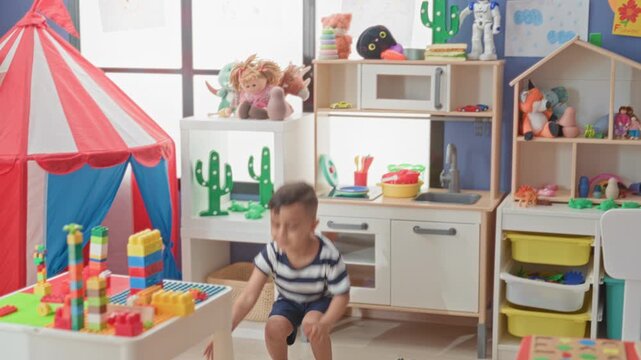 Little boy holds foam plane above head in preschool classroom with play tent and block table; joyful imagination.