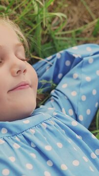 A girl is resting in soft grass wearing a blue polka-dotted dress. The girl s expression is peaceful as she relaxes amidst the green grass and nature.