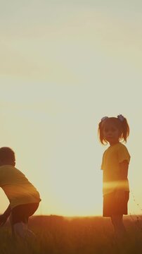 A boy and a girl play in a field at sunset. The boy in a yellow shirt and the girl with pigtails enjoy the warm golden light together.