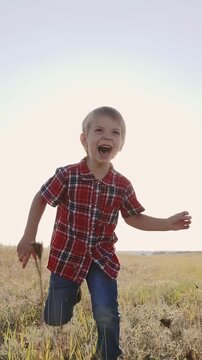 A young boy runs joyfully through a grassy field, smiling widely. The boy wears a checkered shirt and appears playful against the bright sky.