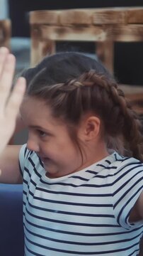 A girl with braided hair is playfully interacting with others, creating a lively atmosphere. The girl laughs as she reaches out to give high-fives in a cheerful environment.