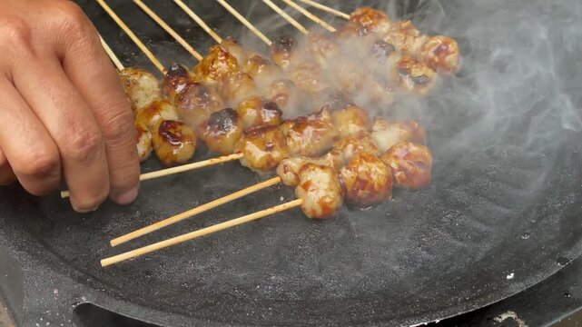 Close up of delicious meatball skewers grilling on a hot plate with smoke