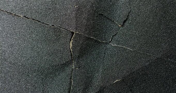 Cracked dark texture. Close-up rough granular surface with deep cracks, slow subtle camera movement. Ideal for industrial, urban and natural backgrounds. 