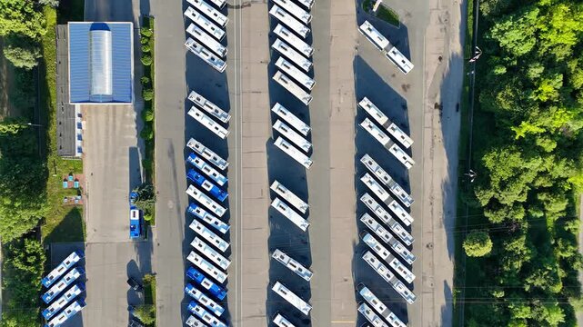 Aerial view of a bus fleet parked in a lot, showcasing a continuous arrangement of buses with surrounding trees and buildings, highlighting the organized layout and spatial relationships