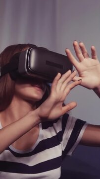 A woman is wearing virtual reality goggles while reaching out with her hands. The woman appears engaged in an immersive virtual reality experience.