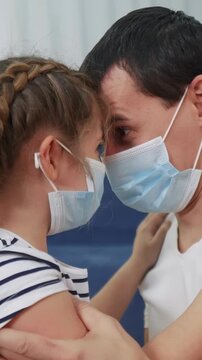 A man and a girl are sharing a close moment while wearing blue masks. Their foreheads touch as they focus on each other, displaying a sense of connection and care.