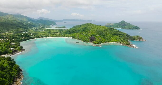 Turquoise bay with calm waters surrounded by lush green hills, white sand beaches, and scattered boats. Seychelles, Mahe.