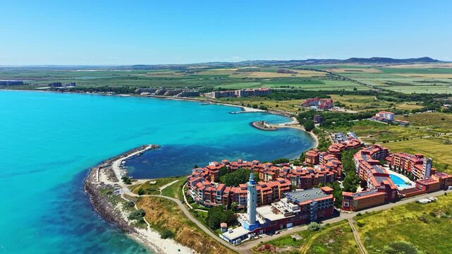 A resort sits along the coast with blue water and green fields. The scene shows the combination of buildings and nature during clear weather with no clouds in sight.