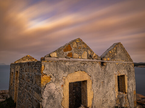 View of the weathered stone ruins of a historic structure overlooking the ocean at dusk with soft clouds in the sky in Torndirrup, Western Australia, Australia.