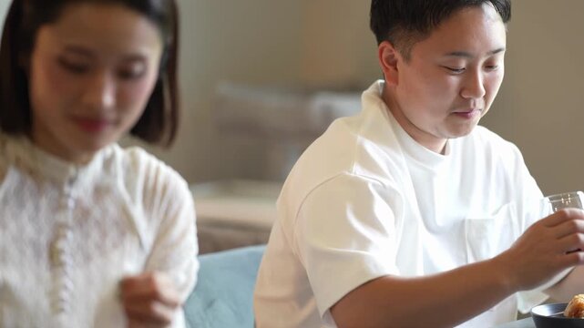 Soft light falls on two people dining quietly. Woman smiles gently, eyes soft, focused on her meal. Man sips drink, head tilted, relaxed and content