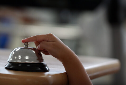 Close-up of a kid ringing a chrome reception bell call button for attention or service with blurred background.