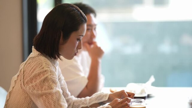 Soft light filters through glass windows. Woman in knit top eats quietly, focused on food. Man beside her rests chin on hand, thoughtful. Warm tones suggest relaxed, intimate dining