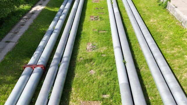 Aerial view of industrial pipes for gas, water, and oil running parallel across a green landscape, showcasing their weathered surfaces and surrounding vegetation in a natural setting