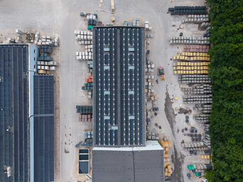 Aerial view of a paving stone factory featuring solar panels on the roof and organized stacks of construction materials in the yard, Riga, Latvia.
