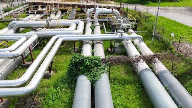 Aerial view of interconnected industrial pipes with green grass and walkways visible, showcasing the complex layout of a facility's piping system in an industrial setting