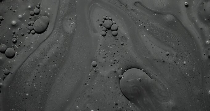 Abstract dark fluid texture. Macro view of viscous gray liquid with bubbles and organic swirls, slow gentle flow creating glossy reflections.