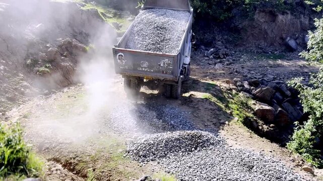 Dump Truck Spreading Gravel on Under Construction Road for Highway Infrastructure Development, Civil Engineering and Road Building Project Progress